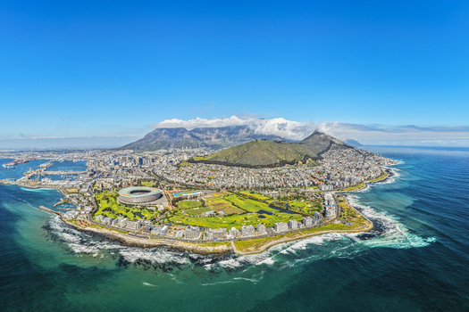 Aerial view of the Cape Town coastline featuring Table Mountain the Cape Town Stadium and urban development under a clear blue sky in Cape Town Western Cape South Africa.