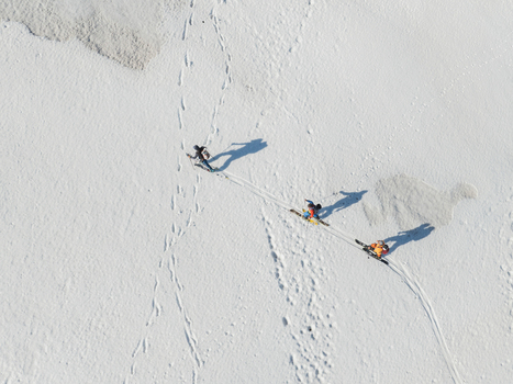 Aerial view of three skiers trekking across a pristine snow covered slope on Mount Etna leaving tracks and long shadows on the white surface Nicolosi Sicilia Italy. Aerial view of three skiers trekking across a pristine snow covered slope on Mount Etna leaving tracks and long shadows on the white surface Nicolosi Sicilia Italy.
