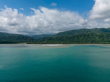 Aerial view of the lush coastline featuring turquoise waters dense tropical rainforests covering the mountains and a sandy beach in Costa Rica.