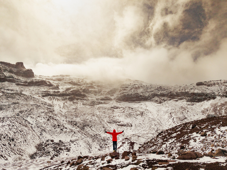 Aerial view of a person in a red jacket standing with arms outstretched on the snowy rocky slopes of Volcano Chimborazo in Guano Chimborazo Ecuador. Aerial view of a person in a red jacket standing with arms outstretched on the snowy rocky slopes of Volcano Chimborazo in Guano Chimborazo Ecuador.