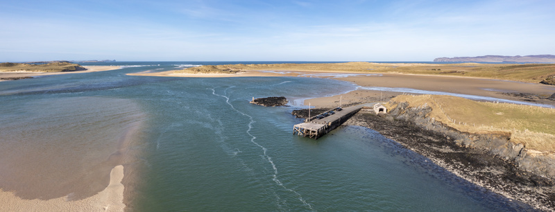 Aerial view of Ballyness Bay featuring a stone pier extending into the turquoise waters surrounded by sandy dunes and rugged coastal landscape in Ballyness County Donegal Ireland. Aerial view of Ballyness Bay featuring a stone pier extending into the turquoise waters surrounded by sandy dunes and rugged coastal landscape in Ballyness County Donegal Ireland.
