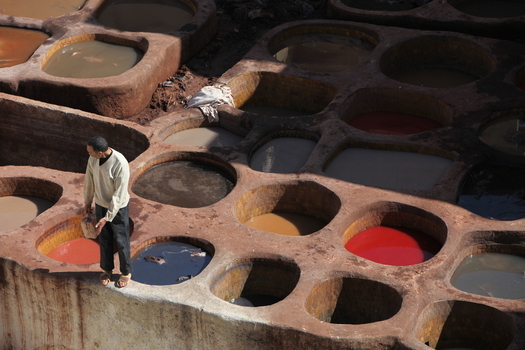 View of a worker standing by traditional stone dye vats in a tannery in Morocco.