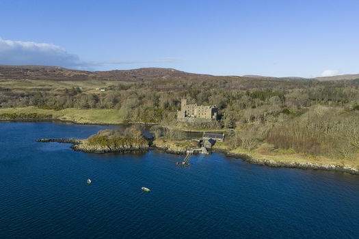 Aerial view of Dunvegan Castle and Gardens perched on a rocky outcrop overlooking the blue waters of Loch Dunvegan in Isle of Skye Scotland United Kingdom. Aerial view of Dunvegan Castle and Gardens perched on a rocky outcrop overlooking the blue waters of Loch Dunvegan in Isle of Skye Scotland United Kingdom.