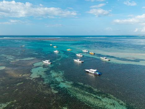 Aerial view of several speedboats and small vessels anchored in the clear turquoise waters of the coral reef under a bright blue sky in Kecamatan Denpasar Selatan Bali Indonesia.