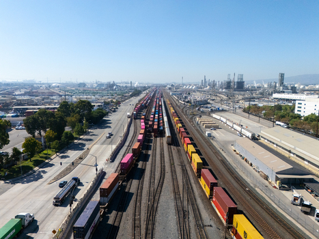 Aerial view of a busy rail yard with multiple freight trains carrying colorful shipping containers surrounded by industrial infrastructure and roads in Carson California United States.