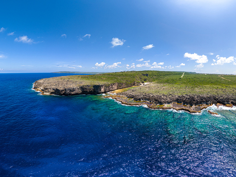 Aerial view of Chigit Beach with rugged cliffs turquoise reef waters and lush vegetation in Northern Tinian Tinian Northern Mariana Islands. Aerial view of Chigit Beach with rugged cliffs turquoise reef waters and lush vegetation in Northern Tinian Tinian Northern Mariana Islands.