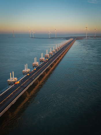 Aerial view of the Oosterscheldekering storm surge barrier with wind turbines and a coastal road during sunset in Vrouwenpolder Zeeland Netherlands.