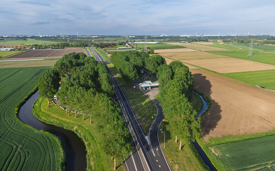 Aerial view of a road passing through lush green agricultural fields and a gas station nestled among tall trees in Vierpolders South Holland Netherlands. Aerial view of a road passing through lush green agricultural fields and a gas station nestled among tall trees in Vierpolders South Holland Netherlands.
