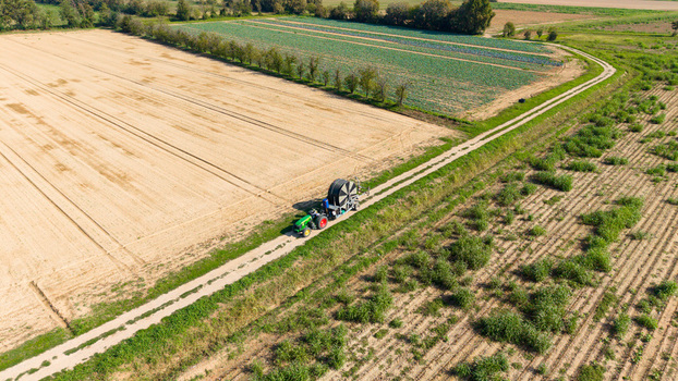 Aerial view of a green tractor pulling a large reel irrigation system along a dirt path through cultivated agricultural fields in Milan Lombardy Italy. Aerial view of a green tractor pulling a large reel irrigation system along a dirt path through cultivated agricultural fields in Milan Lombardy Italy.
