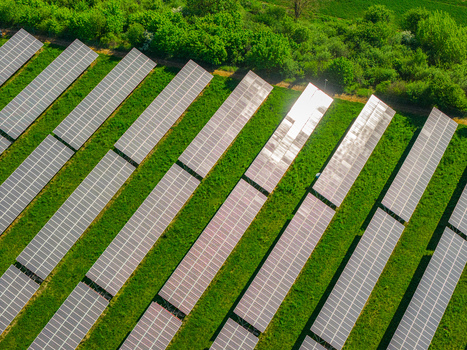 Aerial view of solar panels arranged in rows on a green field bordered by lush trees under bright sunlight Kyjov South Moravian Region Czechia.