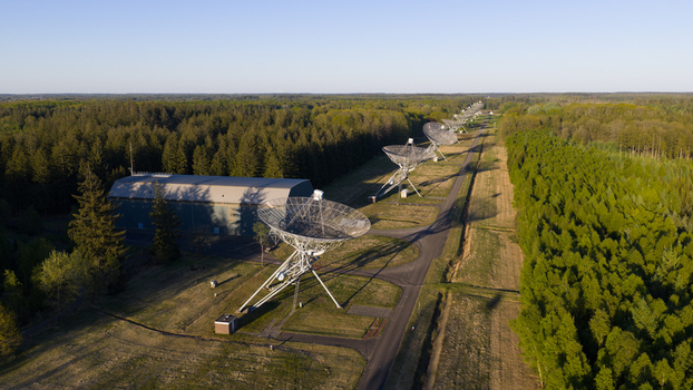 Aerial view of the Westerbork Synthesis Radio Telescope dishes aligned in a row amidst a dense green forest under a clear sky in Zwiggelte Drenthe Netherlands. Aerial view of the Westerbork Synthesis Radio Telescope dishes aligned in a row amidst a dense green forest under a clear sky in Zwiggelte Drenthe Netherlands.