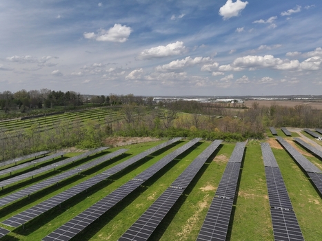 Lebanon United States 12 April 2026 Aerial view of rows of solar panels in a large solar farm surrounded by green fields and trees under a cloudy sky.