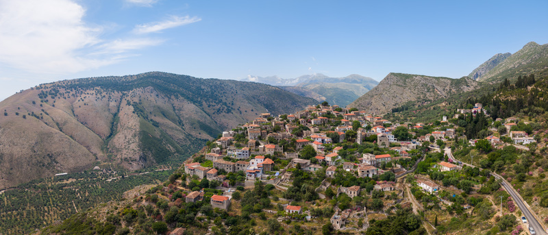 Aerial view of historic stone houses and red tiled roofs of Qeparo Fshat village on a lush hillside against rugged mountains in Qeparo Fshat Vlore County Albania. Aerial view of historic stone houses and red tiled roofs of Qeparo Fshat village on a lush hillside against rugged mountains in Qeparo Fshat Vlore County Albania.