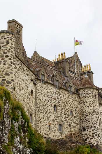 View of Duart Castle featuring its historic stone walls turrets and a flag flying against an overcast sky on the Isle of Mull Scotland United Kingdom.