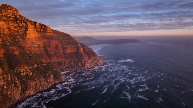 Aerial view of the rugged cliffs of Chapman s Peak Drive overlooking the Atlantic Ocean during a vibrant sunset with waves crashing against the shore in Cape Town Western Cape South Africa. Aerial view of the rugged cliffs of Chapman s Peak Drive overlooking the Atlantic Ocean during a vibrant sunset with waves crashing against the shore in Cape Town Western Cape South Africa.
