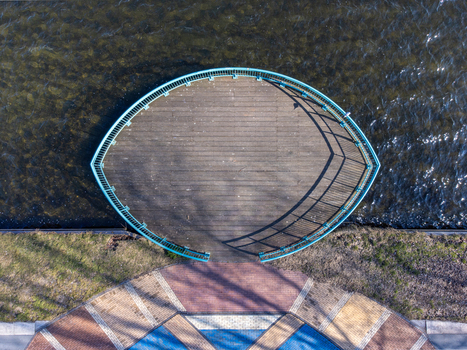 Aerial view of a curved wooden platform with a blue railing overlooking the shimmering water and abstract patterns below Maastrichtkwartier Flevoland Netherlands. Aerial view of a curved wooden platform with a blue railing overlooking the shimmering water and abstract patterns below Maastrichtkwartier Flevoland Netherlands.