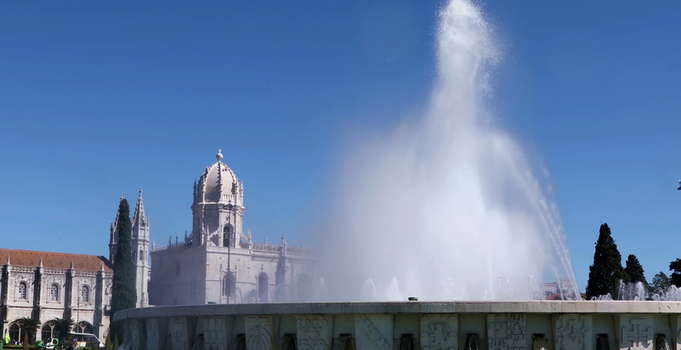View of the historic Jeronimos Monastery with a large fountain spraying water in the foreground under a clear blue sky in Lisboa Lisboa Portugal. View of the historic Jeronimos Monastery with a large fountain spraying water in the foreground under a clear blue sky in Lisboa Lisboa Portugal.