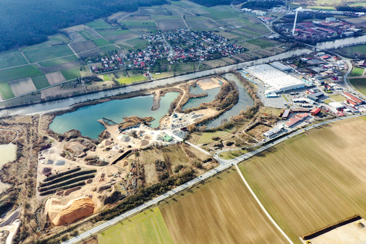 Aerial view of a gravel pit and industrial site next to the river canal surrounded by green fields and residential areas in Forchheim Bavaria Germany. Aerial view of a gravel pit and industrial site next to the river canal surrounded by green fields and residential areas in Forchheim Bavaria Germany.