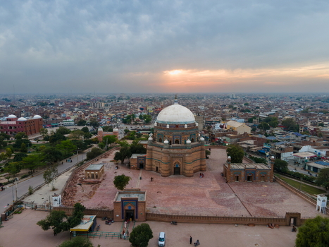 Aerial view of the historic Tomb of Shah Rukn e Alam with its large white dome and brickwork set amidst the urban landscape of Multan during a golden sunset in Multan Punjab Pakistan.