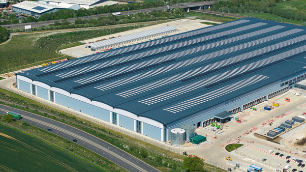 Aerial view of Symmetry Park distribution center featuring a large modern warehouse with loading bays and solar panels near the A14 road in Kettering England United Kingdom. Aerial view of Symmetry Park distribution center featuring a large modern warehouse with loading bays and solar panels near the A14 road in Kettering England United Kingdom.