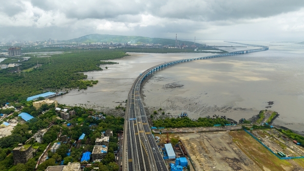 Aerial view of the Atal Bihari Vajpayee Sewri Nhava Sheva Atal Setu bridge spanning the bay with lush mangroves industrial skyline and cloudy sky in Mumbai Maharashtra India. Aerial view of the Atal Bihari Vajpayee Sewri Nhava Sheva Atal Setu bridge spanning the bay with lush mangroves industrial skyline and cloudy sky in Mumbai Maharashtra India.