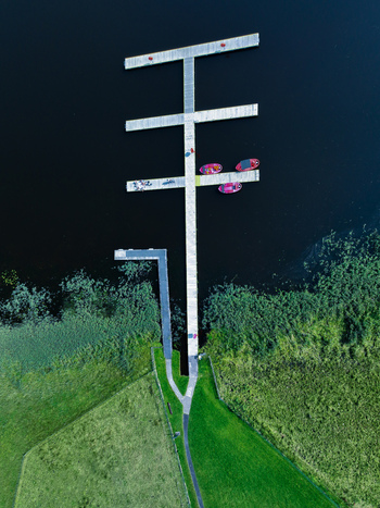 Aerial view of a wooden pier extending into a lake with small red boats moored alongside surrounded by lush green grassy banks and reeds in Enniskillen Northern Ireland United Kingdom.