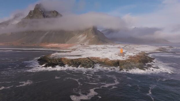 Aerial view of an orange lighthouse on a snowy coast Iceland.