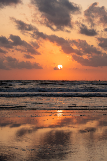 View of Strand Wijk aan Zee at sunset with orange clouds reflecting on the wet sand and waves crashing on the shore in Wijk aan Zee North Holland Netherlands. View of Strand Wijk aan Zee at sunset with orange clouds reflecting on the wet sand and waves crashing on the shore in Wijk aan Zee North Holland Netherlands.