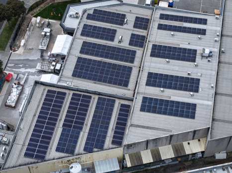 Melbourne VIC Australia 25 September 2026 Aerial view of a large industrial factory roof covered with solar panel arrays featuring white temporary structures and surrounding infrastructure.
