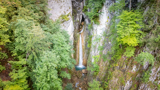 Aerial view of Grandvillard Waterfall cascading through a narrow rocky gorge surrounded by dense green forest and steep cliffs Grandvillard Fribourg Switzerland.