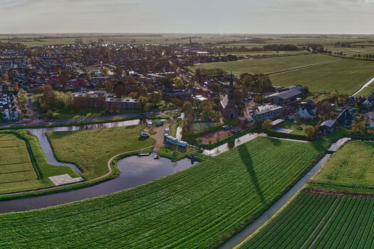 Aerial view of the village center of Spanbroek featuring a tall church spire surrounded by lush green fields and winding canals in Spanbroek North Holland Netherlands.