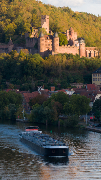 Aerial view of Wertheim Castle overlooking the Main river with a cargo ship sailing past the historic town surrounded by green hills in golden light Wertheim Baden Wurttemberg Germany. Aerial view of Wertheim Castle overlooking the Main river with a cargo ship sailing past the historic town surrounded by green hills in golden light Wertheim Baden Wurttemberg Germany.