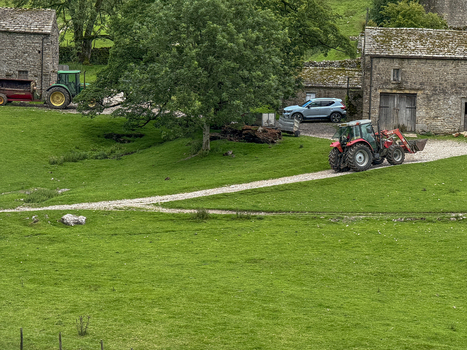 View of a red tractor driving on a gravel path past traditional stone farm buildings and green pastures in Hawes England United Kingdom. View of a red tractor driving on a gravel path past traditional stone farm buildings and green pastures in Hawes England United Kingdom.