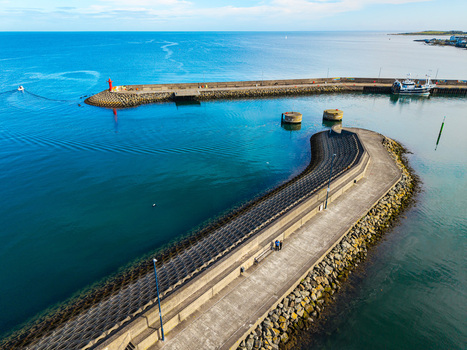 Aerial view of Bangor Harbour and Town with its stone breakwaters calm blue waters a small boat and people walking along the pier in Bangor Northern Ireland United Kingdom.