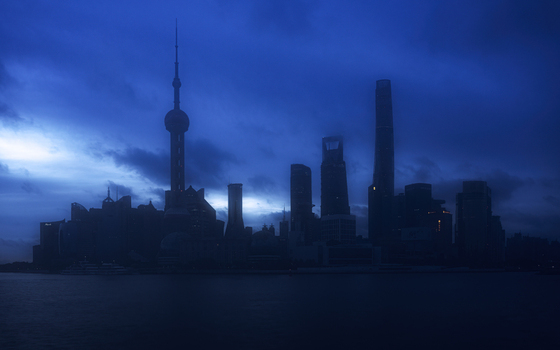 View of the Shanghai skyline at dusk featuring the Oriental Pearl Tower and Shanghai Tower silhouetted against a deep blue sky over the Huangpu River in Shanghai Shanghai China.