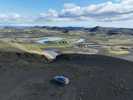 Aerial view of Langisjor campsite with a parked SUV on volcanic terrain overlooking the turquoise lake and mossy hills in Kirkjubaejaklaustur Skaftarhreppur Iceland.