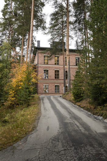 View of a historic brick building nestled among tall pine trees with a paved driveway leading to the entrance in Jyvaskyla Central Finland Finland.