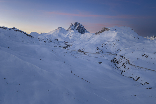 Aerial view of the snow covered Pyrenees mountains at dusk with a winding road cutting through the landscape under a soft pink and blue sky Spain. Aerial view of the snow covered Pyrenees mountains at dusk with a winding road cutting through the landscape under a soft pink and blue sky Spain.
