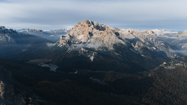 Aerial view of Monte Cristallo mountain range overlooking forested valleys and a small alpine lake under a soft sky in the Dolomites Auronzo di Cadore Veneto Italy. Aerial view of Monte Cristallo mountain range overlooking forested valleys and a small alpine lake under a soft sky in the Dolomites Auronzo di Cadore Veneto Italy.