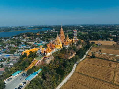 Aerial view of the ornate golden pagodas and chedis of Wat Tham Suea temple complex on a lush hilltop overlooking rice fields and the river in Muang Chum Kanchanaburi Thailand. Aerial view of the ornate golden pagodas and chedis of Wat Tham Suea temple complex on a lush hilltop overlooking rice fields and the river in Muang Chum Kanchanaburi Thailand.