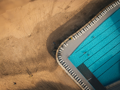 Aerial view of the saltwater swimming pool at Praia Grande with blue water lane lines and white lounge chairs on the golden sand beach in Colares Lisbon Portugal.