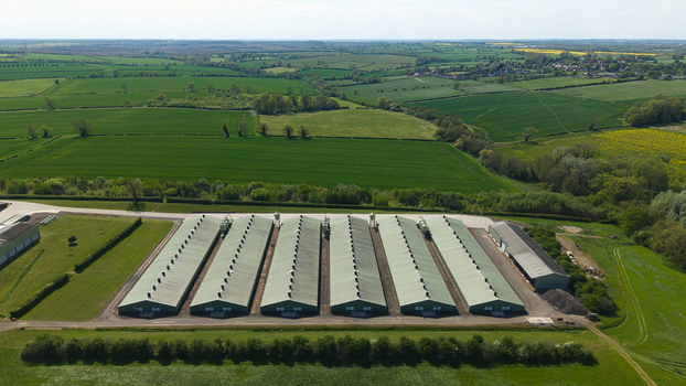 Aerial view of large industrial farm buildings with long green roofs surrounded by lush green agricultural fields and trees under a bright sky in Kettering England United Kingdom. Aerial view of large industrial farm buildings with long green roofs surrounded by lush green agricultural fields and trees under a bright sky in Kettering England United Kingdom.