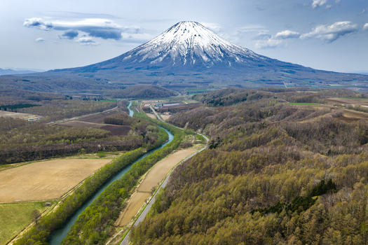 Aerial view of Mount Yotei rising above the lush spring landscape with a winding river and agricultural fields in Niseko Hokkaido Japan.