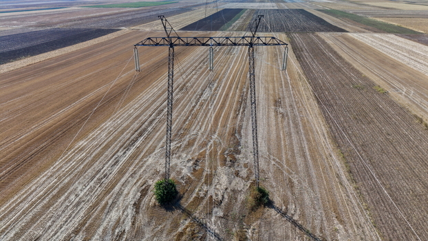 Aerial view of electric power transmission lines standing in a vast harvested agricultural field in Pancevo Serbia.