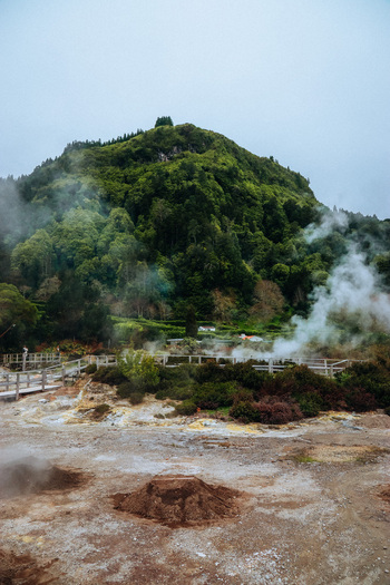 View of geothermal activity releases ethereal steam amidst a landscape of vibrant greens and earth tones creating a surreal and captivating scene Furnas Azores Portugal.