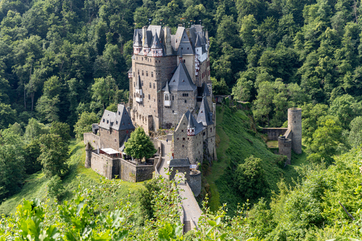 View of Eltz Castle with its medieval stone architecture multiple turrets and a stone bridge surrounded by a dense green forest in Wierschem Rhineland Palatinate Germany.