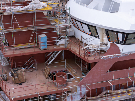 Aerial view of a large ship under construction in a shipyard with extensive scaffolding surrounding the metal hull and white bridge in Gdansk Poland. Aerial view of a large ship under construction in a shipyard with extensive scaffolding surrounding the metal hull and white bridge in Gdansk Poland.
