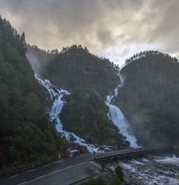 Aerial view of Latefossen twin waterfall cascading down rocky cliffs with a stone bridge and lush forest under a cloudy sky Skare Vestland Norway.
