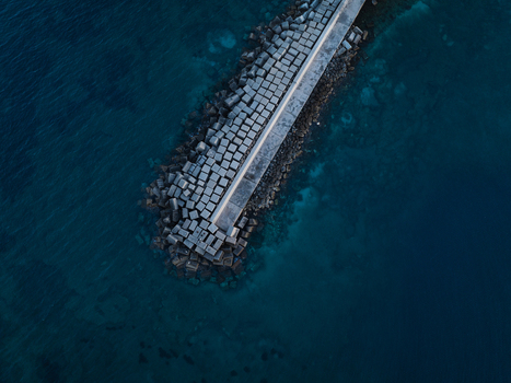 Aerial view of the concrete block breakwater protecting the coast of the Island of Ortigia surrounded by deep blue sea water in Syracuse Sicily Italy. Aerial view of the concrete block breakwater protecting the coast of the Island of Ortigia surrounded by deep blue sea water in Syracuse Sicily Italy.