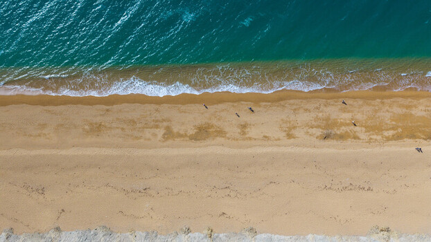 Aerial view of West Bay beach with golden sand turquoise sea waves washing the shore and people walking along the coastline in West Bay England United Kingdom. Aerial view of West Bay beach with golden sand turquoise sea waves washing the shore and people walking along the coastline in West Bay England United Kingdom.